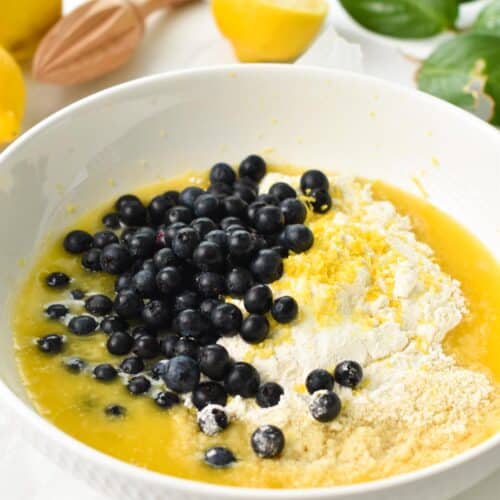 a mixing bowl filled with flour, almond flour, melted butter, lemon zest, blueberries