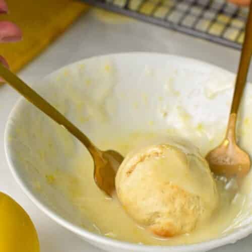 two forks holding a lemon donut hole in a bowl filled with lemon glazing
