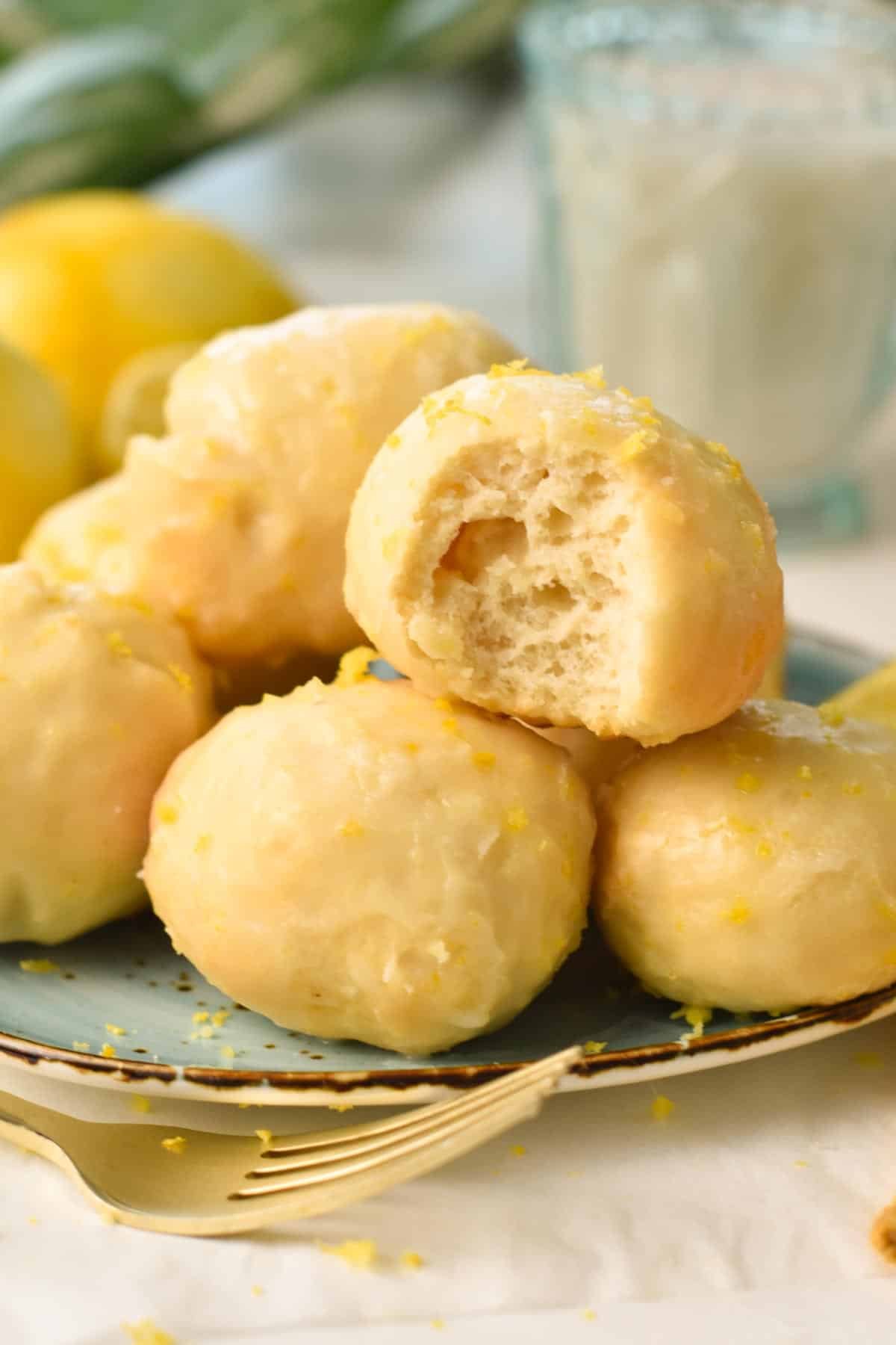A stack of lemon glazed donut holes with the one on top half beaten showing the fluffy texture of the dough.