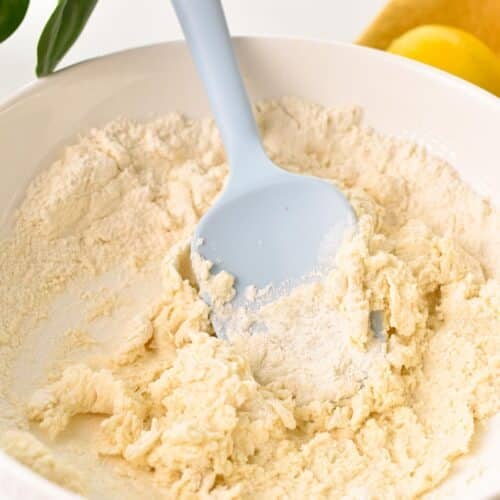 a mixing bowl with a light blue silicone spatula and a crumbly flour dough