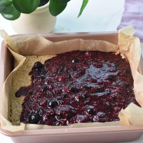 Spreading chia blueberry jam on the Blueberry Breakfast Bars  base in a square pan.