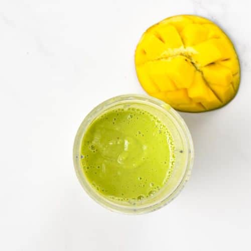 Mango Spinach Smoothie blended in a blender next to a fresh mango.