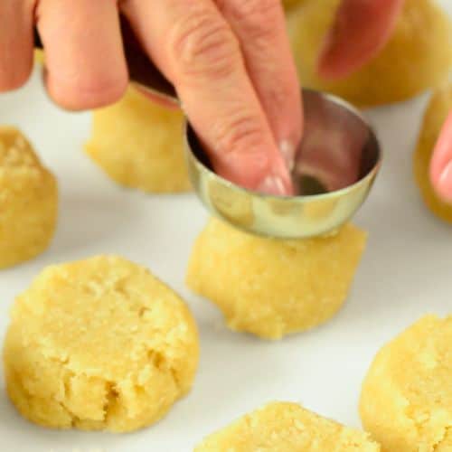 Flattening cookie dough balls with a measuring spoon.