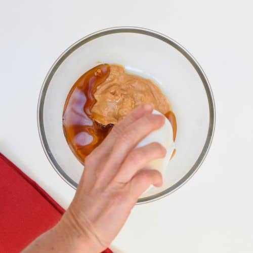 Pouring maple syrup on peanut butter in a large mixing bowl.