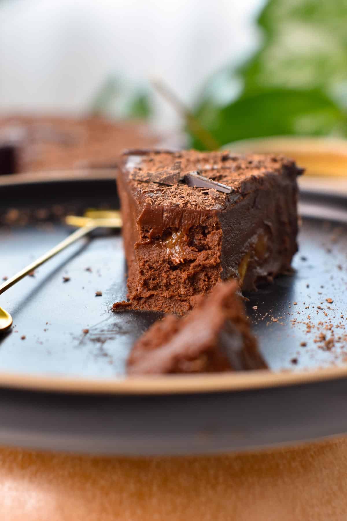 A slice of No Bake Chocolate Cake on a black plate, with a golden fork on the side and the front of the cake slice half cut.