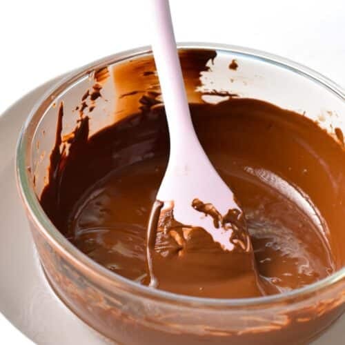 melted chocolate in a glass bowl with a pink silicone spatula in the bowl