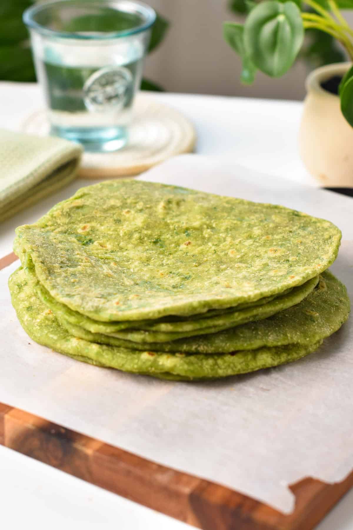 A stack of green spinach tortillas on a chopping board covered with white parchment paper.
