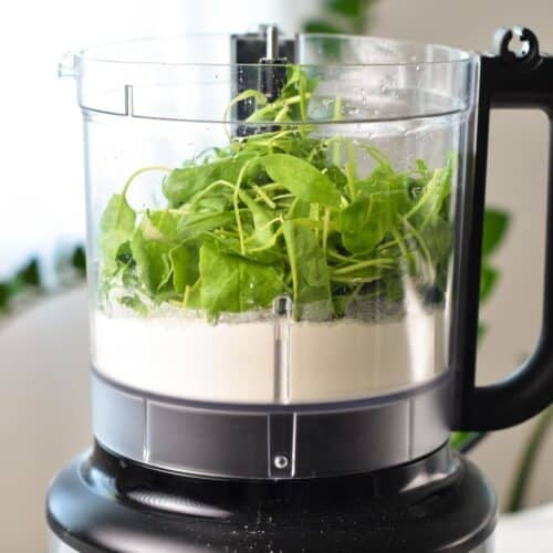 A food processor bowl filled with flour, fresh spinach olive oil and water.