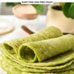 a stack of green spinach tortillas on a chopping board covered with white parchment paper, and the two tortillas on top rolled