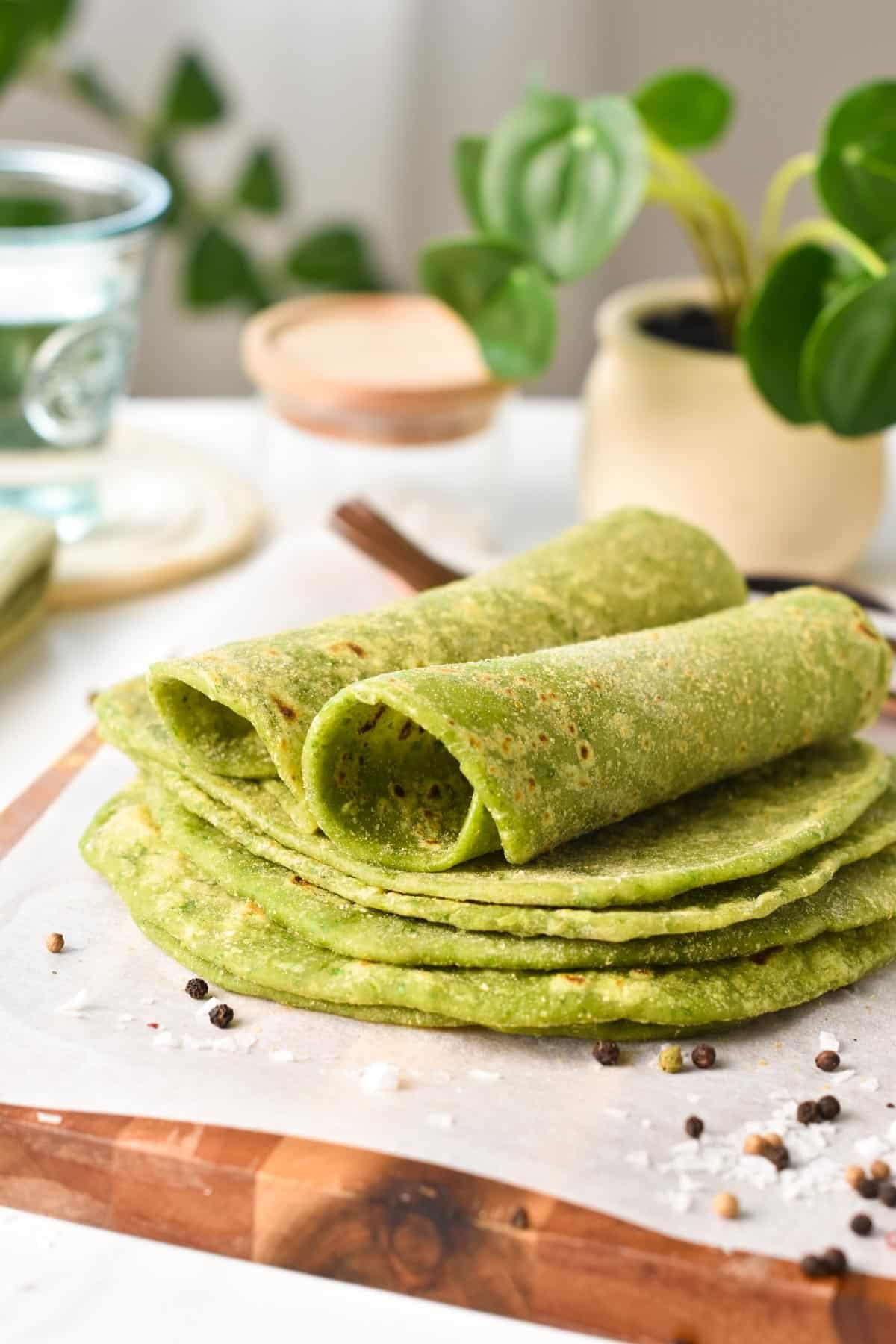 A stack of green spinach tortillas on a chopping board covered with white parchment paper, and the two tortillas on top rolled.
