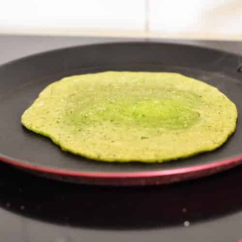 A green tortilla cooking in a skillet.