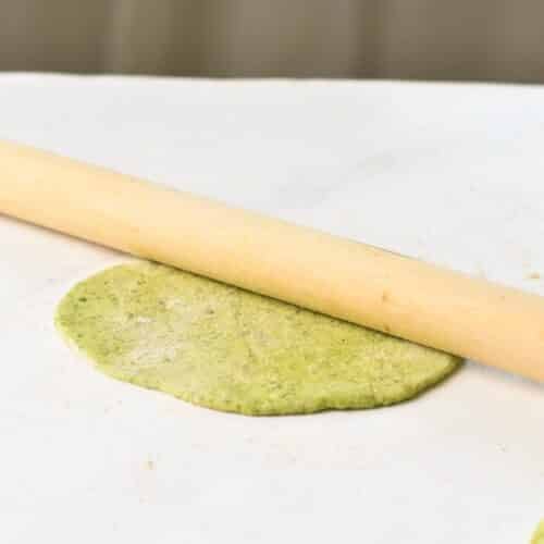 A wooden roller pin on a green tortilla dough.