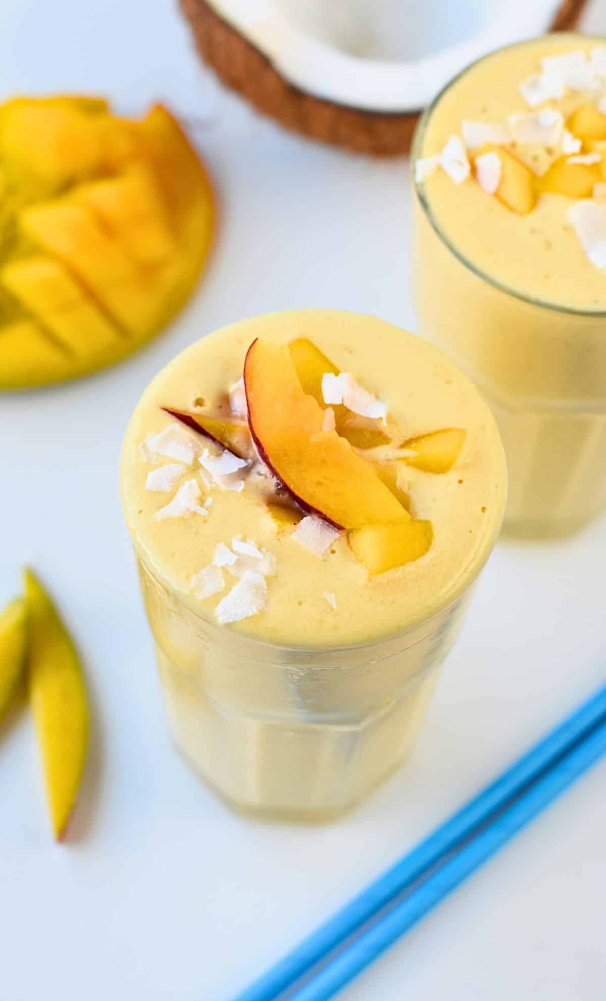 Vegan mango smoothie in a tall glass with a peach slice.