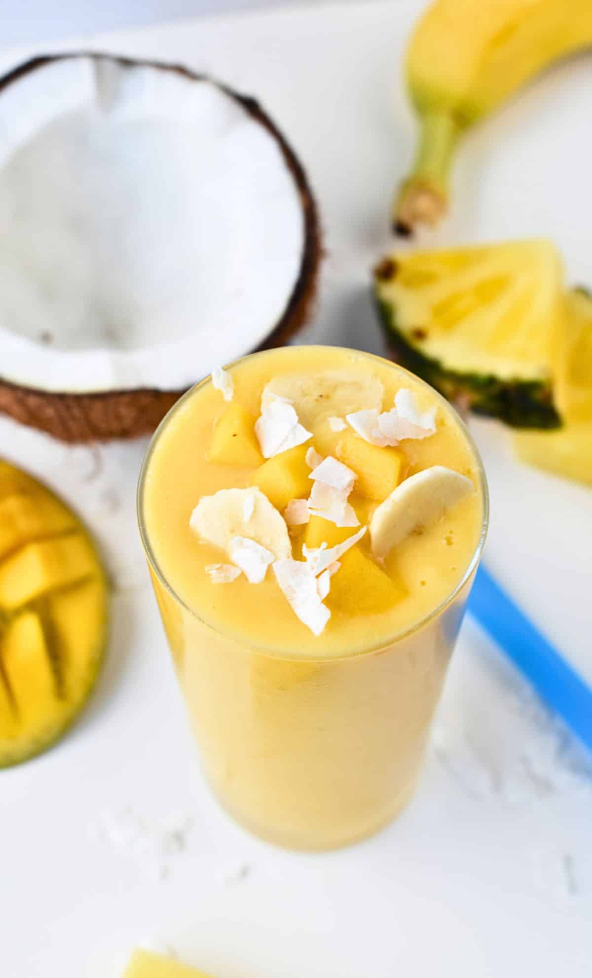 Vegan Tropical Smoothie in a large glass decorated with coconut flakes and banana slices.