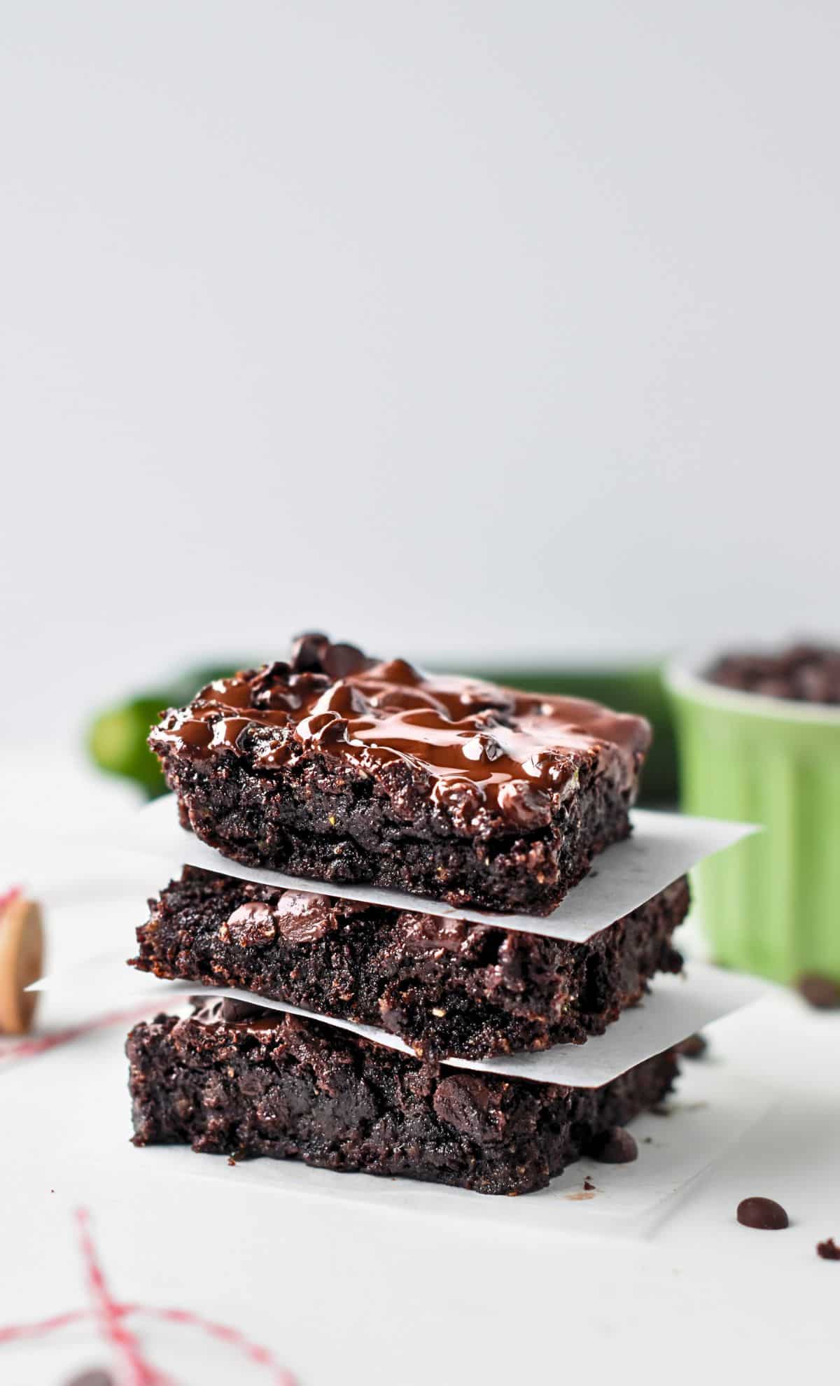 Vegan Zucchini Brownies stacked on a table separated with baking paper.