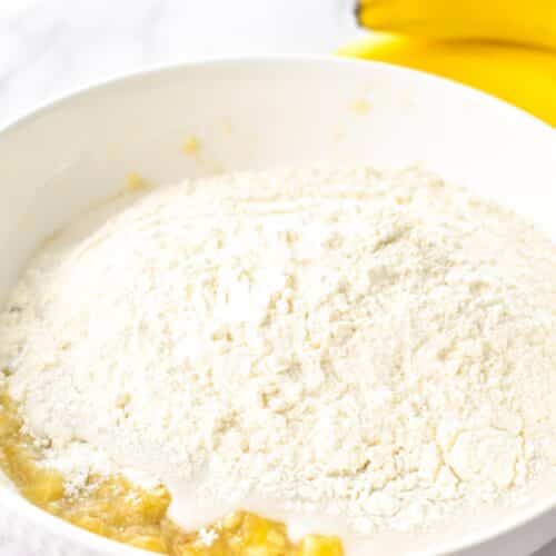 A mixing bowl with mashed banana, flour, and condensed milk.