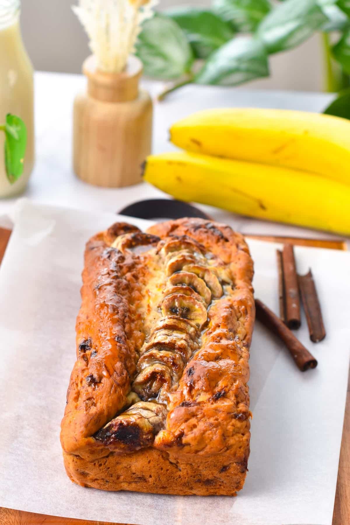 A banana bread on a chopping board with banana slices on top.