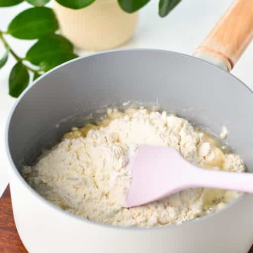 a rubber spatula in a non-stick saucepan filled with flour and boiled water and a green plant in the back