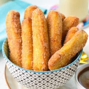 a bowl filled with golden air fryer churros coated with cinnamon sugar and a blue towel in the background