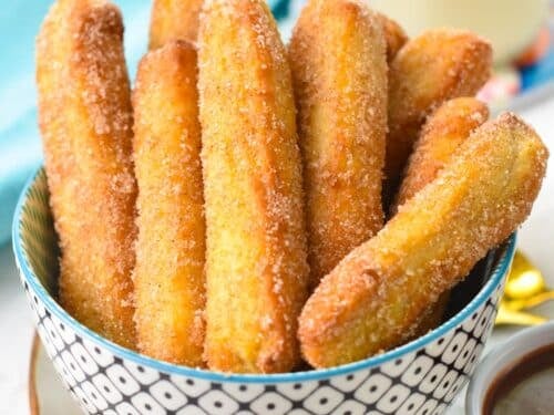 a bowl filled with golden air fryer churros coated with cinnamon sugar and a blue towel in the background