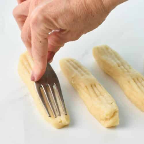 a hand holding a fork and marking churros dough by pressing the fork on logs of dough