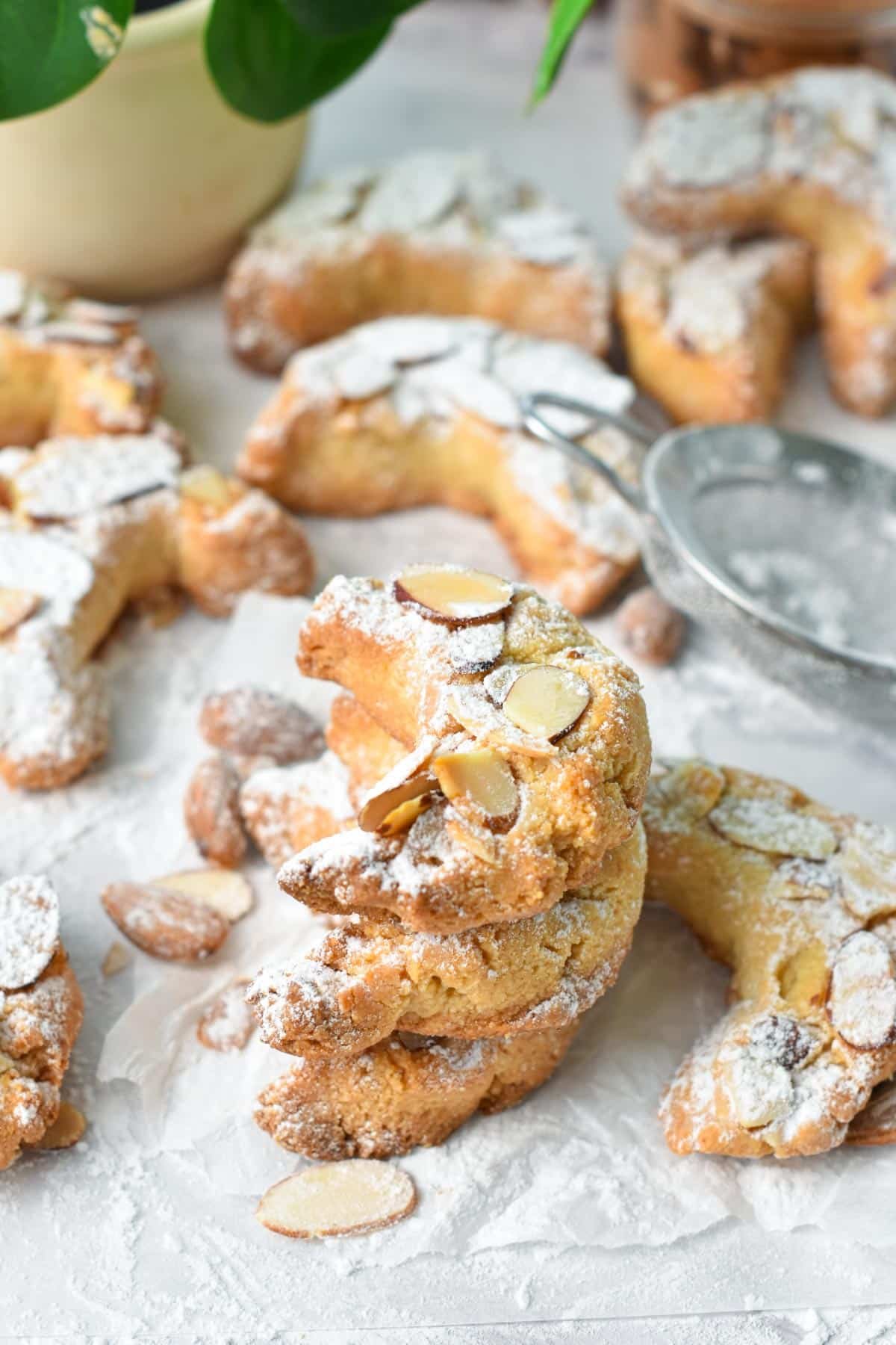 A stack of almond shaped croissant cookies with toasted sliced almonds on top and a dust of powdered sugar.