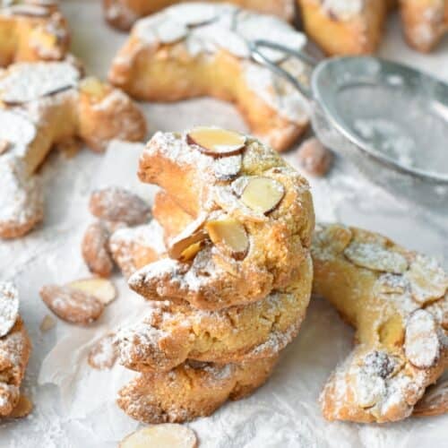 a stack of almond shaped croissant cookies with toasted sliced almonds on top and a dust of powdered sugar