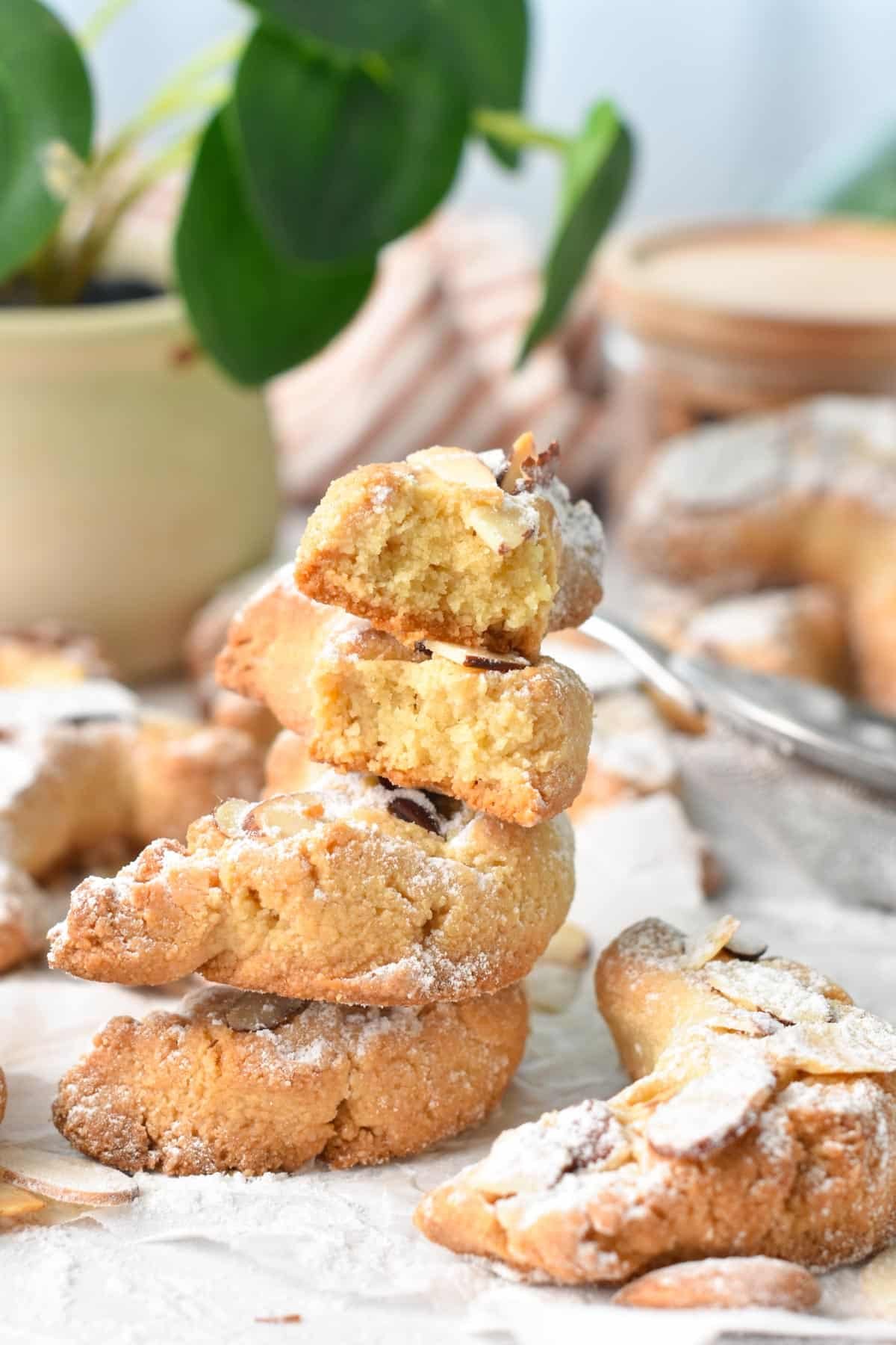 A stack of almond flour croissant shaped cookies with the two on top half broken showing the buttery texture of the cookie.