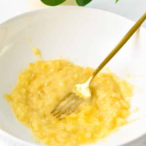 Mashed bananas in a mixing bowl with a golden fork.