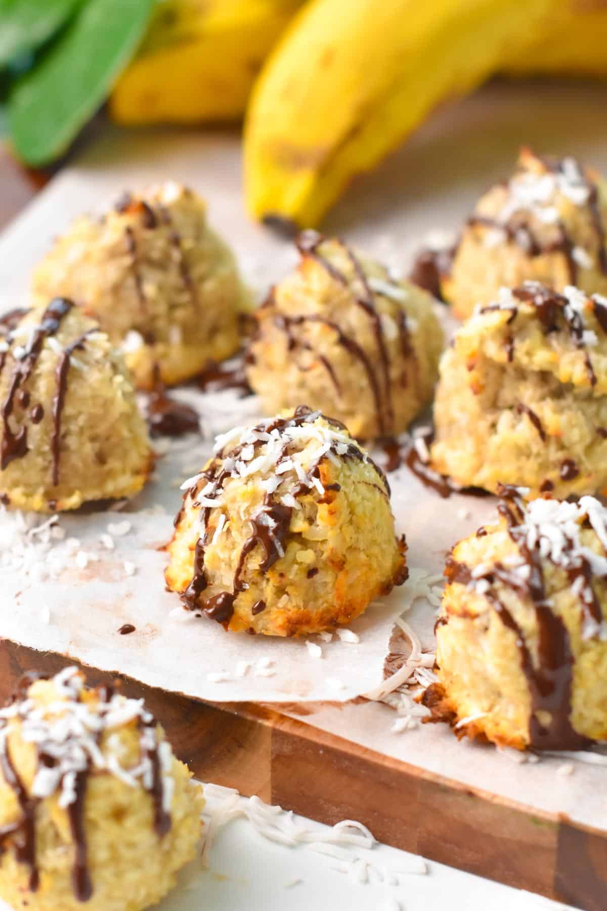 some coconut banana cookies with chocolate drizzle on top, on a wooden board covered with white parchment paper