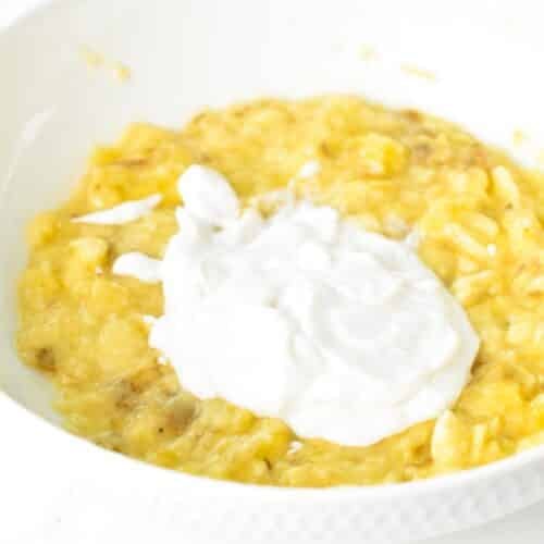 A mixing bowl with mashed bananas and yogurt.