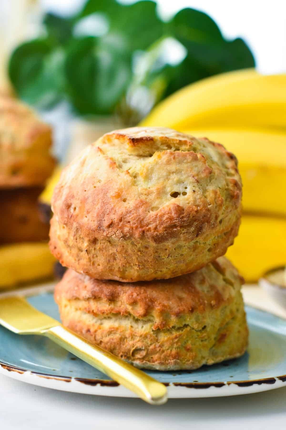 two bananas scones stacked, on a blue plate and a yellow knife on side.