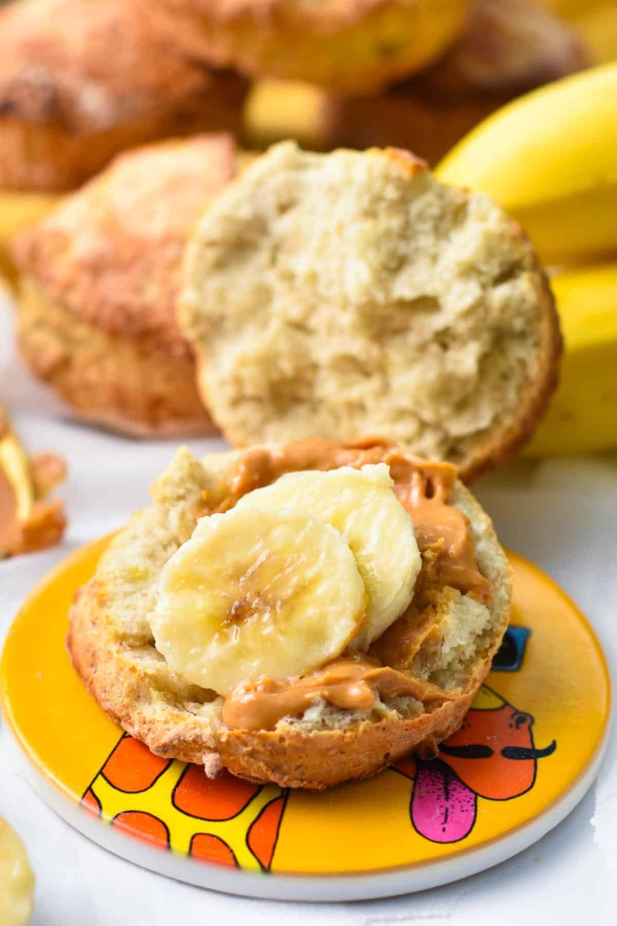 A banana scone half open with one of the half covered with peanut butter and 2 slices of bananas.