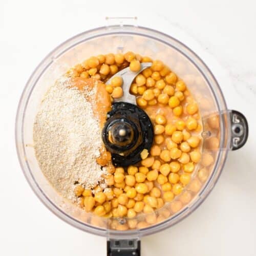 a food processor bowl picture from the top filled with chickpeas, oat flour, maple syrup, vanilla extract, and  peanut butter