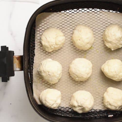 Air fryer donut holes ready to cook in an air fryer basket.