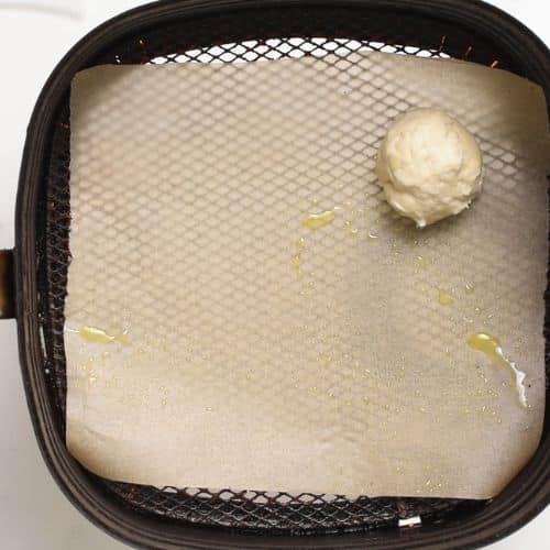 An air fryer donut hole placed in an air fryer basket.