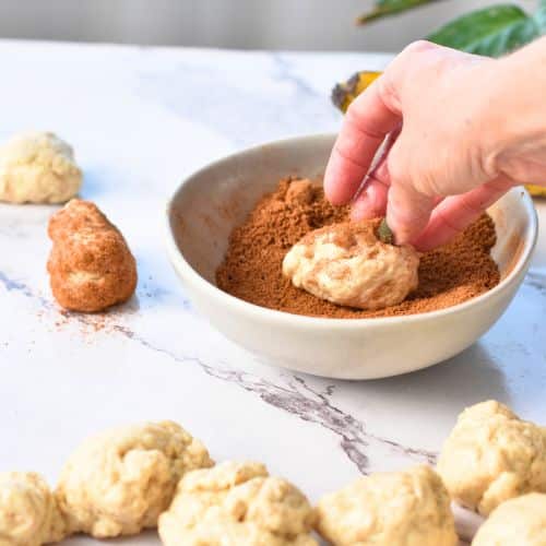 Rolling banana monkey bread dough ball in cinnamon sugar mixture.