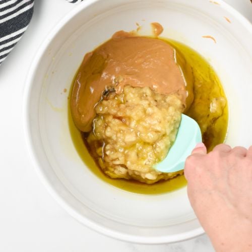 Stirring mashed banana with oil and peanut butter.