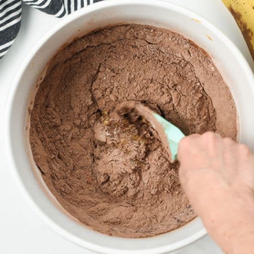 Combining the chocolate peanut butter banana bread batter in a large mixing bowl with a silicone spatula.