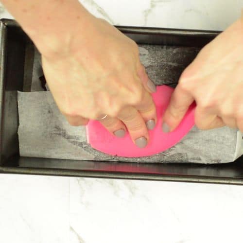 Flattening the no-bake brownies in a loaf pan with a silicone spatula.