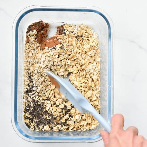 Stirring dry Nutella overnight oats ingredients in a container with a silicone spatula.