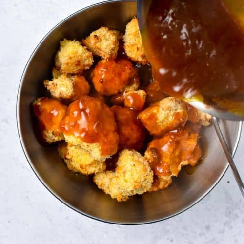 Pouring the vegan orange sauce on top of crumbed cauliflower florets in a large mixing bowl. 