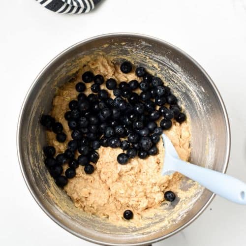 Fresh blueberries on the Protein Blueberry Muffin batter in a mixing bowl.