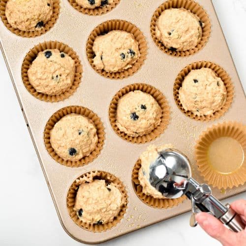 Pouring the Protein Blueberry Muffins batter into muffin cups with an ice cream scoop.