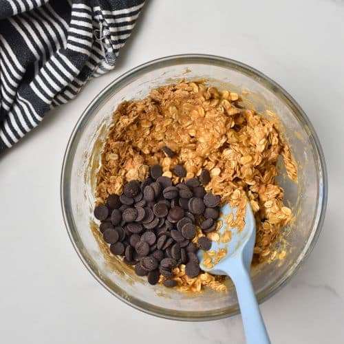 Chocolate chips on the Protein Oatmeal Cookies batter in a mixing bowl with a blue silicone spatula.