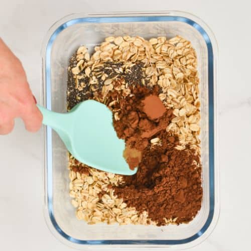 tiramisu overnight oat dry ingredients mixed in a large container with a silicone spatula.