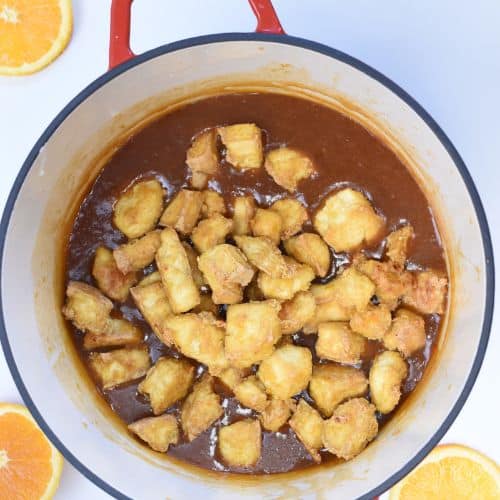 Cooked tofu pieces in the orange sauce in a cast-iron pan.