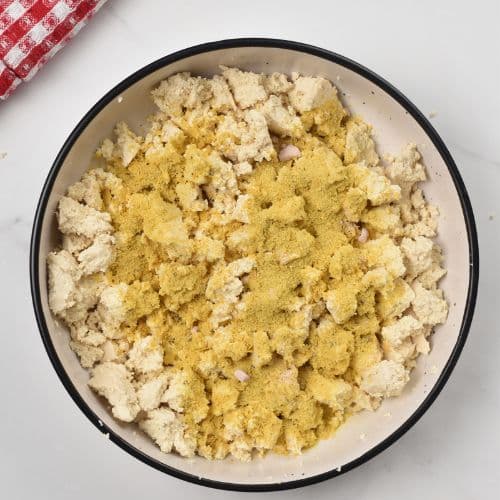 Sprinkling nutritional yeast on crumbled tofu.