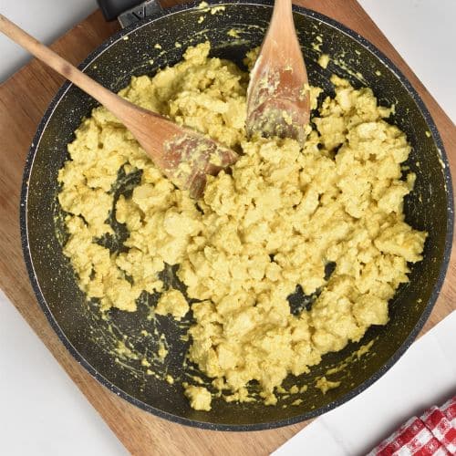 Cooked tofu scramble in a frying pan with two wooden spatula.