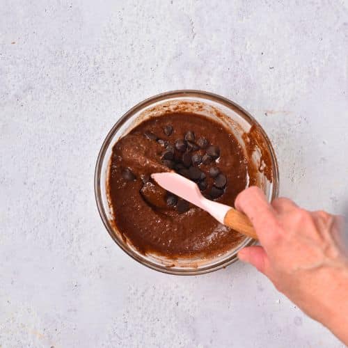 Vegan Gluten-Free Mug Cake batter with chocolate chips in a bowl stirred with a silicone spatula.